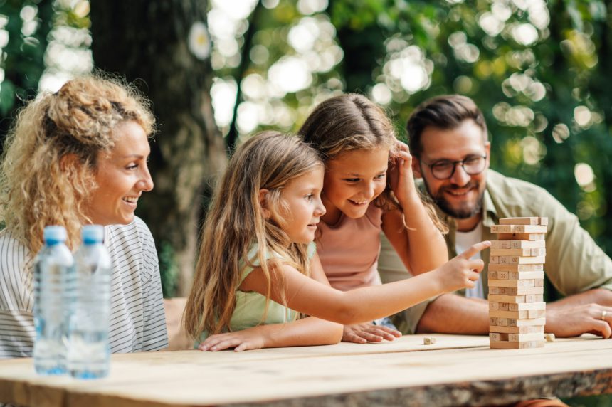 Family is sitting at the table in nature and playing jenga game.