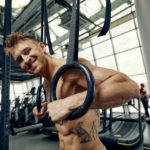 Muscle-up exercise young man doing intense cross fit workout at the gym on gymnastic rings.