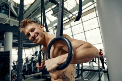 Muscle-up exercise young man doing intense cross fit workout at the gym on gymnastic rings.