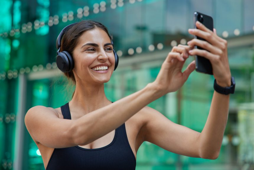 Photo of positive sportswoman in good physical shape wears sportsclothes makes video conference via