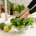 Preparing healthy foods. Woman in sport clothes washing spinach in the kitchen